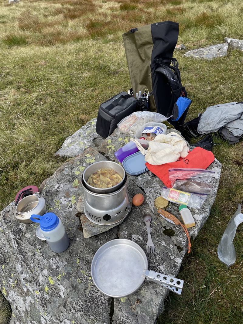 Trangia stove stewing mushrooms, and other camping paraphernalia, on a large stone